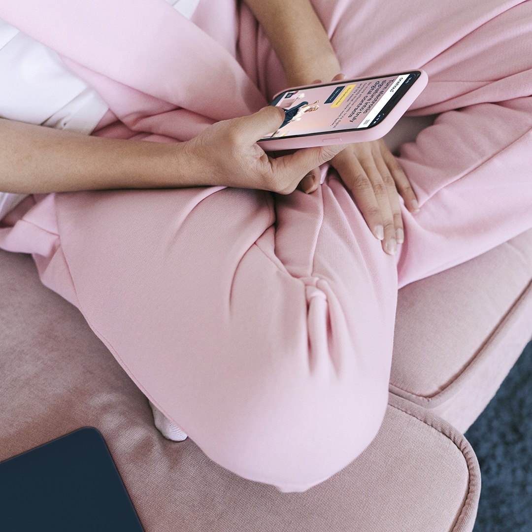 Woman holding phone displaying Oneflow website wearing pink trousers - blog on how Oneflow can help your start-up